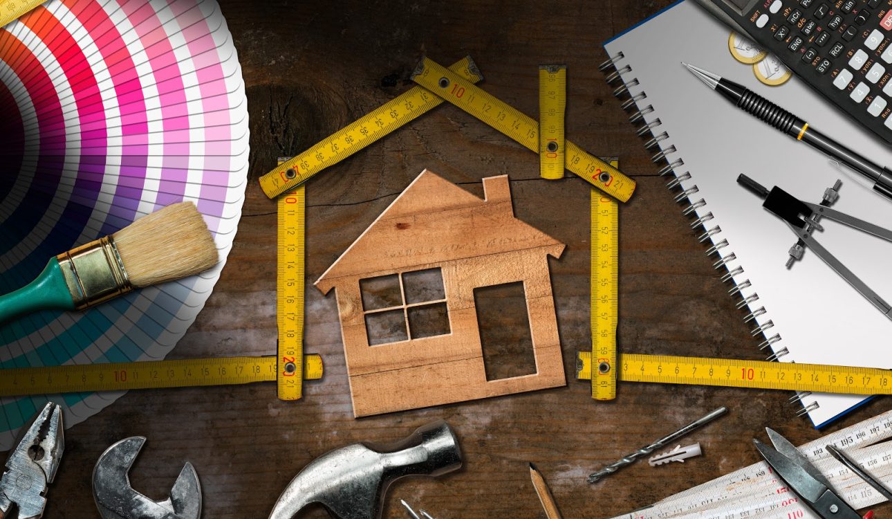 Home improvement concept - Wooden model house with folding ruler, work tools and a calculator on a wooden desk